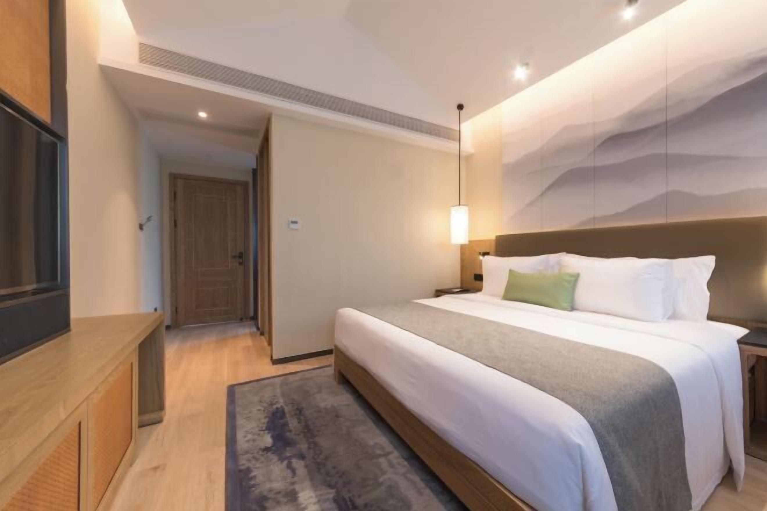 Una habitación de hotel con cama, mesita de noche y televisor sobre un pedestal.