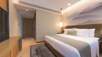 Una habitación de hotel con cama, mesita de noche y televisor sobre un pedestal.