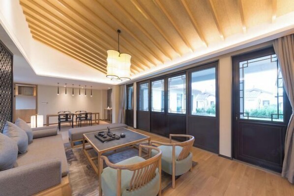 Een moderne woonkamer met een houten plafond, grote ramen, een bank, een eettafel en stoelen.
