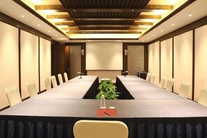 Un salón de conferencias con una mesa larga, sillas, una pantalla de proyector y una planta sobre la mesa.