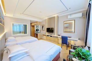 Una habitación de hotel con cama, escritorio, silla, televisor y planta.
