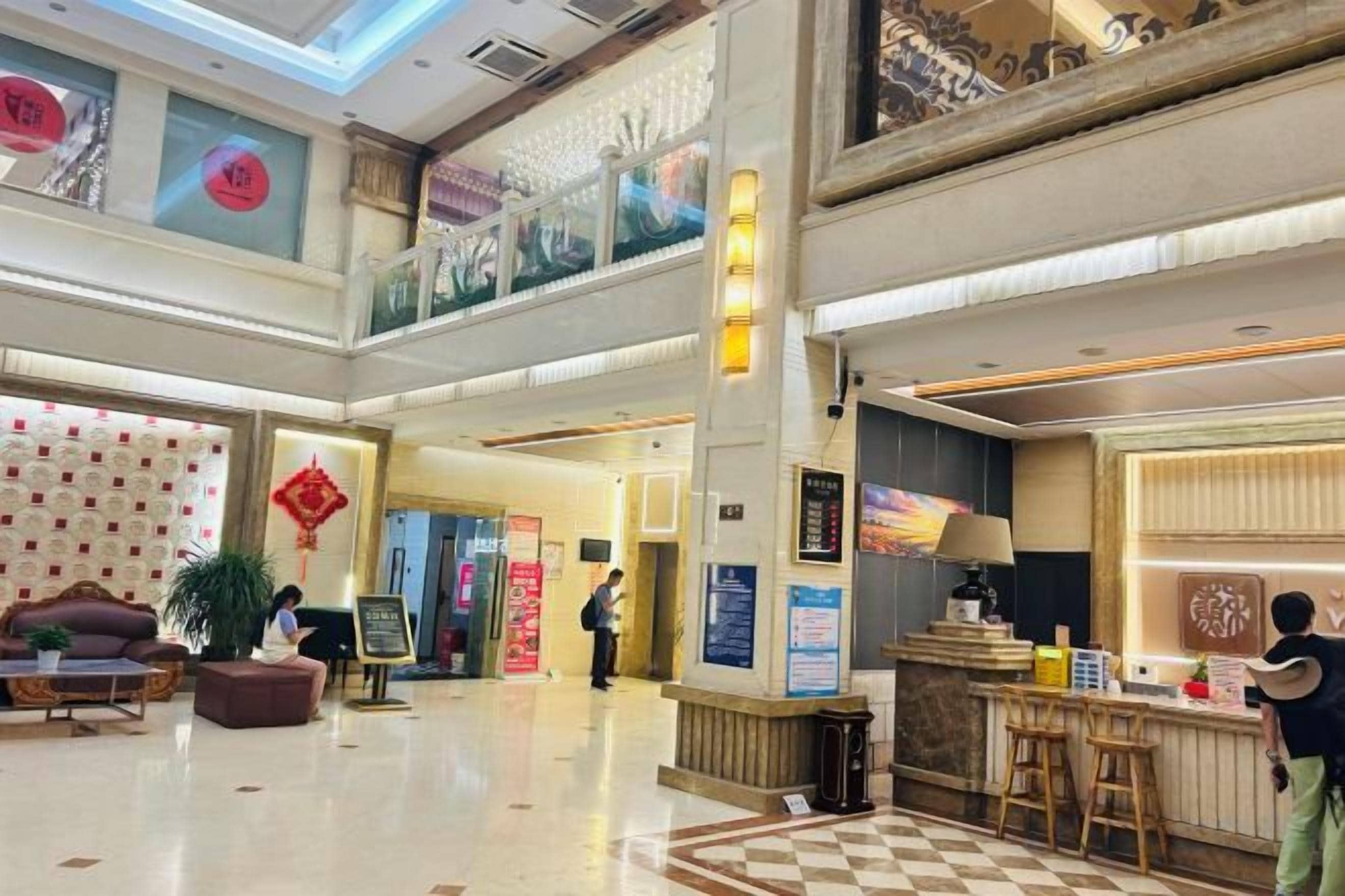 A hotel lobby with a checkered floor, a reception desk, and a staircase leading to an upper level.