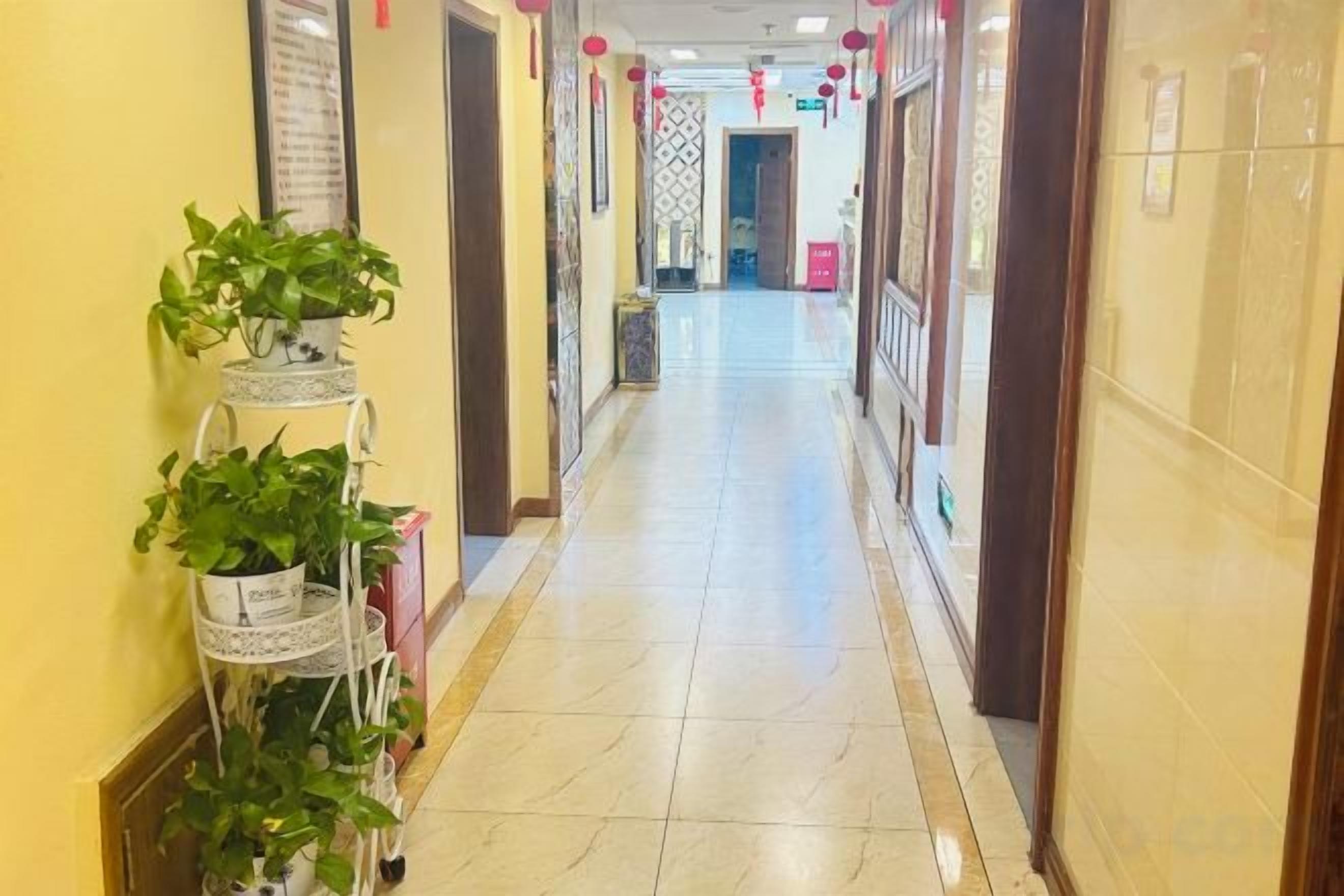 A hotel corridor with a tiled floor, potted plants, and a door at the end.
