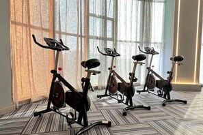 Four stationary bikes arranged in a row in a room with large windows and patterned carpet flooring.