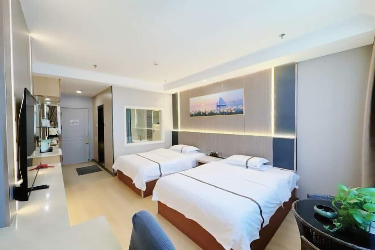 Una camera d'albergo con due letti, una scrivania, una sedia, una TV e un quadro appeso al muro.
