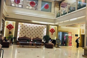 A hotel lobby with a reception desk, seating area, and a decorative wall. - Jiangsu Hotel (Yining City)