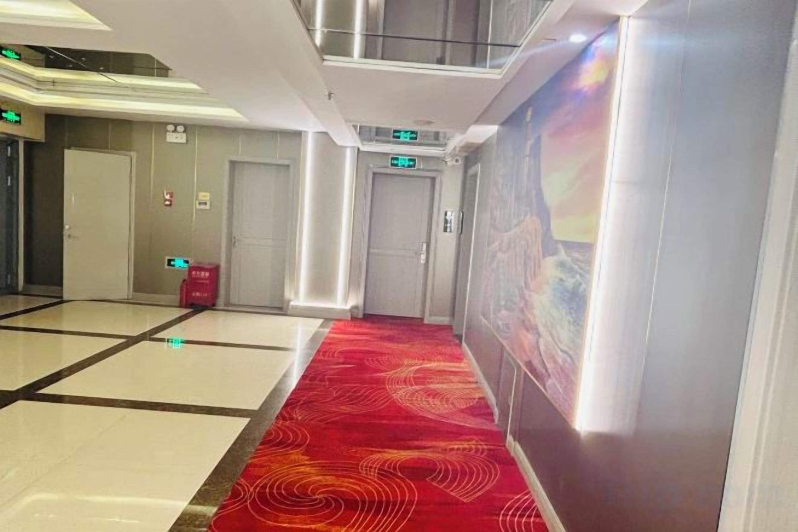 A hotel corridor with a red carpet, white and black tiled floor, and a large poster on the wall.