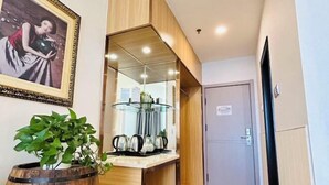 A hallway with a wooden cabinet, a glass-top table with teapots, a potted plant, and a framed picture on the wall. - Jiangsu Hotel (Yining City)