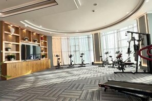 Une salle de sport équipée de vélos d’exercice, d’un tapis de course et d’un téléviseur posé sur un meuble en bois.