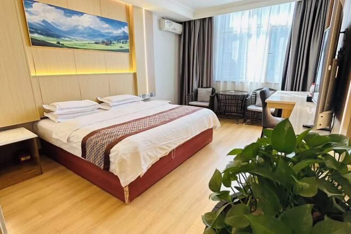 Una camera d'albergo con un letto, una scrivania, una sedia, un tavolo e un'ampia finestra con tende.
