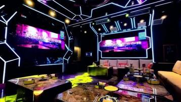 A modern bar area with neon lighting, multiple screens, and bar stools.