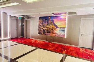 Un vestíbulo de hotel con alfombra roja, un mural de un faro y una puerta blanca.