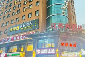 Un immeuble à plusieurs étages abritant divers commerces au rez-de-chaussée, notamment un restaurant et une boutique dont l’enseigne est illuminée.