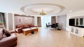 A modern living room with a sofa, coffee table, TV, and dining area. - Jiangsu Hotel (Yining City)
