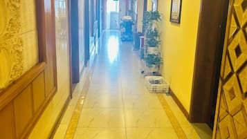 A hotel corridor with a tiled floor, a wooden door on the right, and a plant on the left.