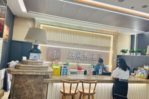 Un comptoir d’accueil à l’hôtel Jiang Su, avec un guichet, des chaises et un réceptionniste.