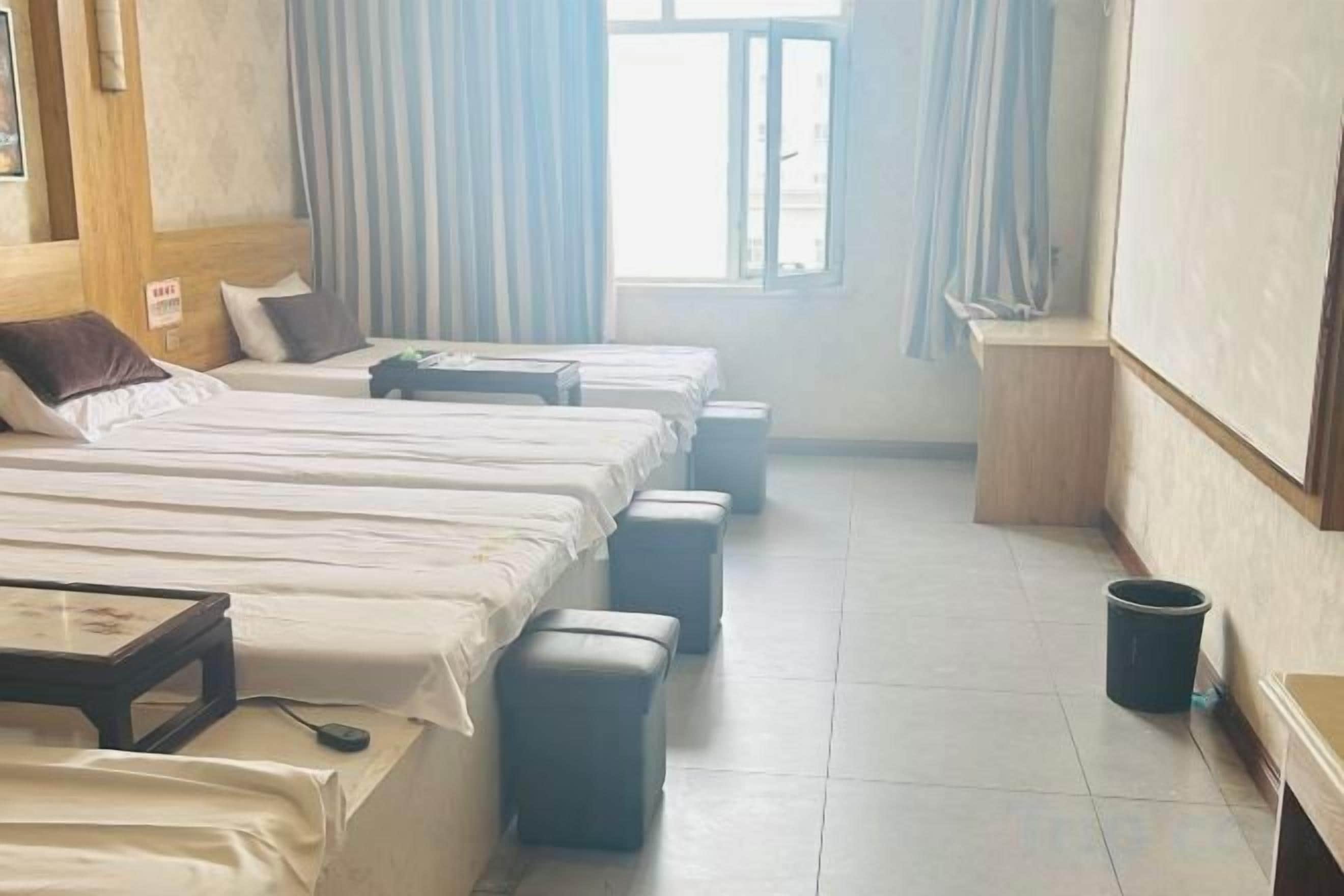 A hotel room with three beds, a wooden headboard, a window with curtains, and a tiled floor.
