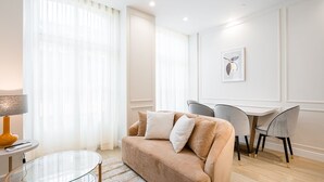A modern living room with a beige sofa, a glass coffee table, and a dining area with a white table and grey chairs. - GuestReady - A charming studio in downtown (Porto)