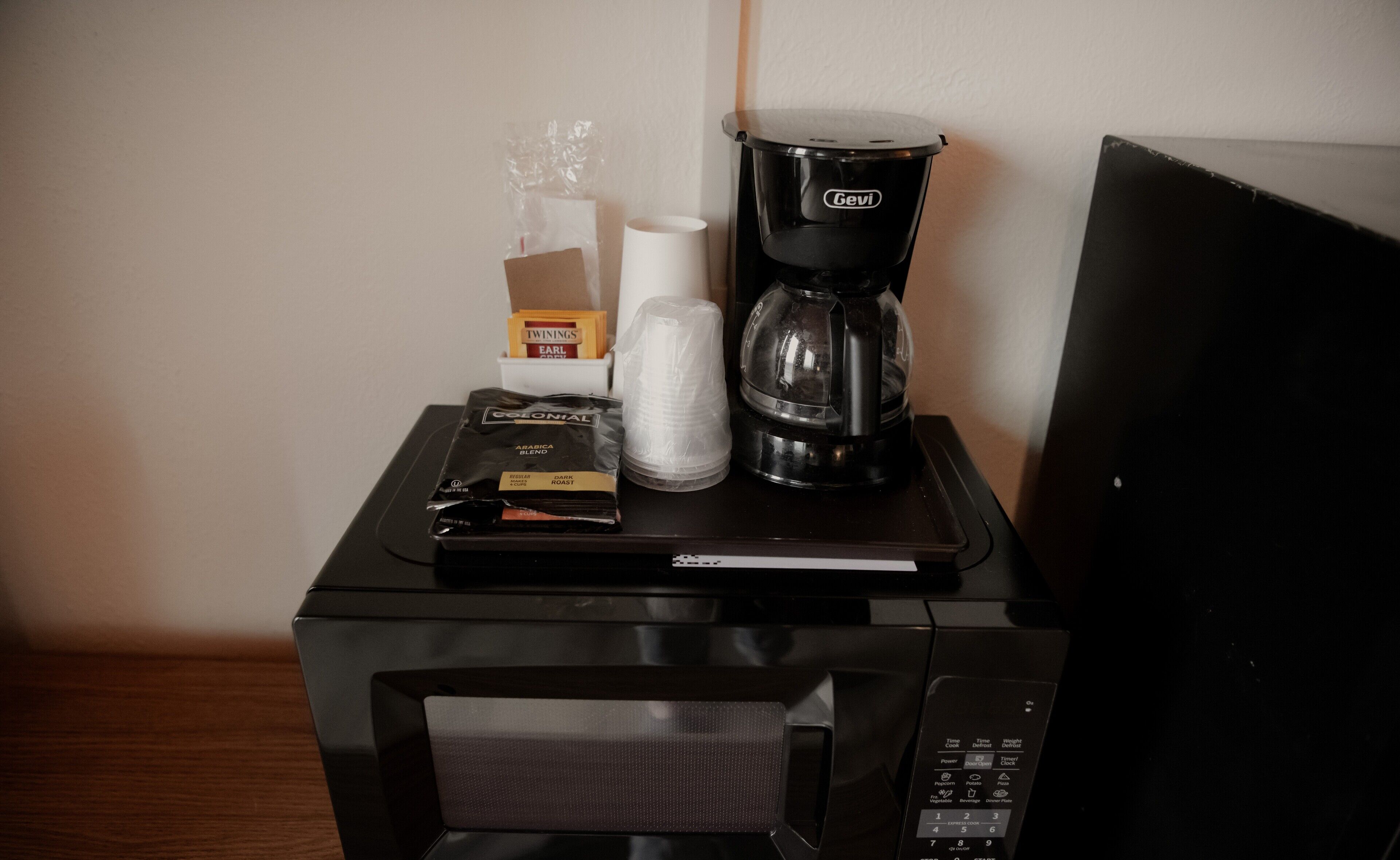 A microwave with a coffee maker and disposable cups on top.