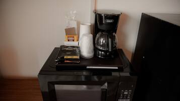 A microwave with a coffee maker and disposable cups on top.