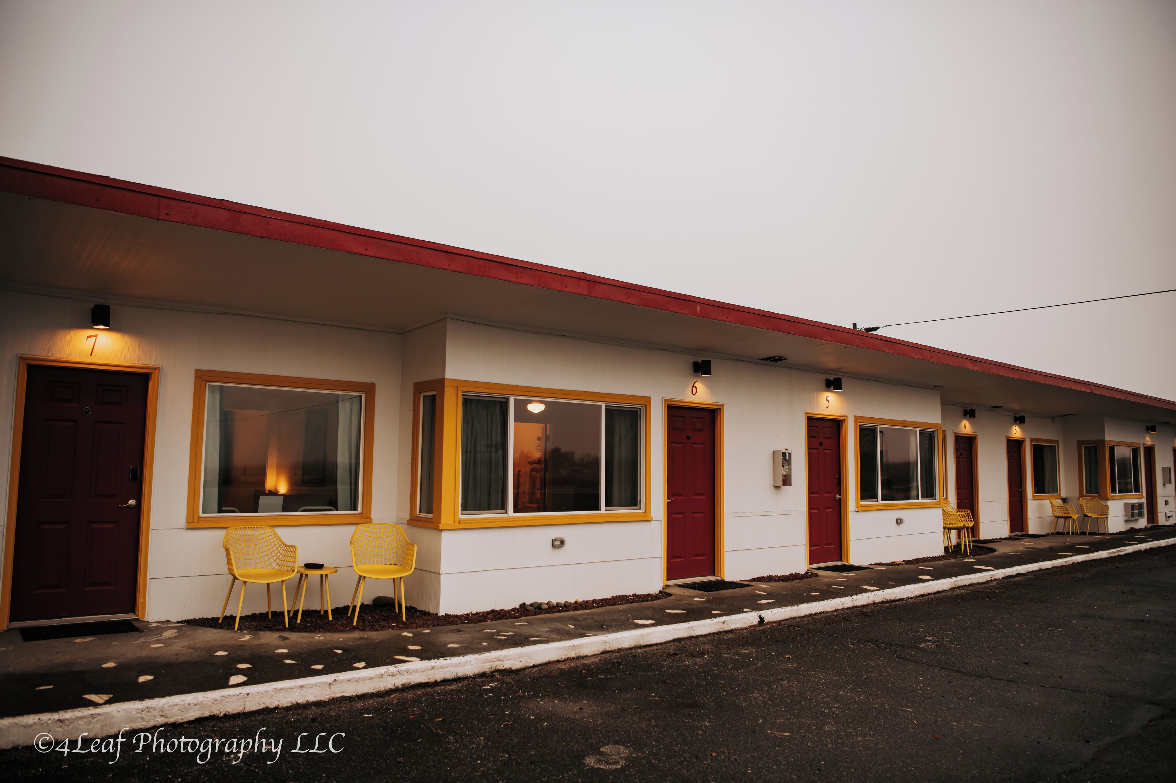 Un motel con diverse camere, ognuna dotata di porta e finestra, e una piccola area esterna con sedute.