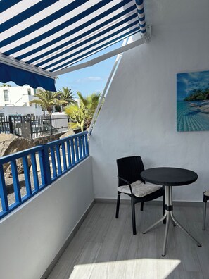 A balcony with a blue railing, a black chair, and a small round table. - Beach II The accommodation is close to the beach, stores, pharmacy, and supermarket.... (Puerto del Carmen)