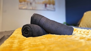 A bed with a yellow blanket and two rolled-up towels.
