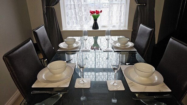 A dining table set for six with black leather chairs, white plates, and clear glassware.