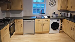 A kitchen with wooden cabinets, a dishwasher, a washing machine, a microwave, and a clock on the wall.