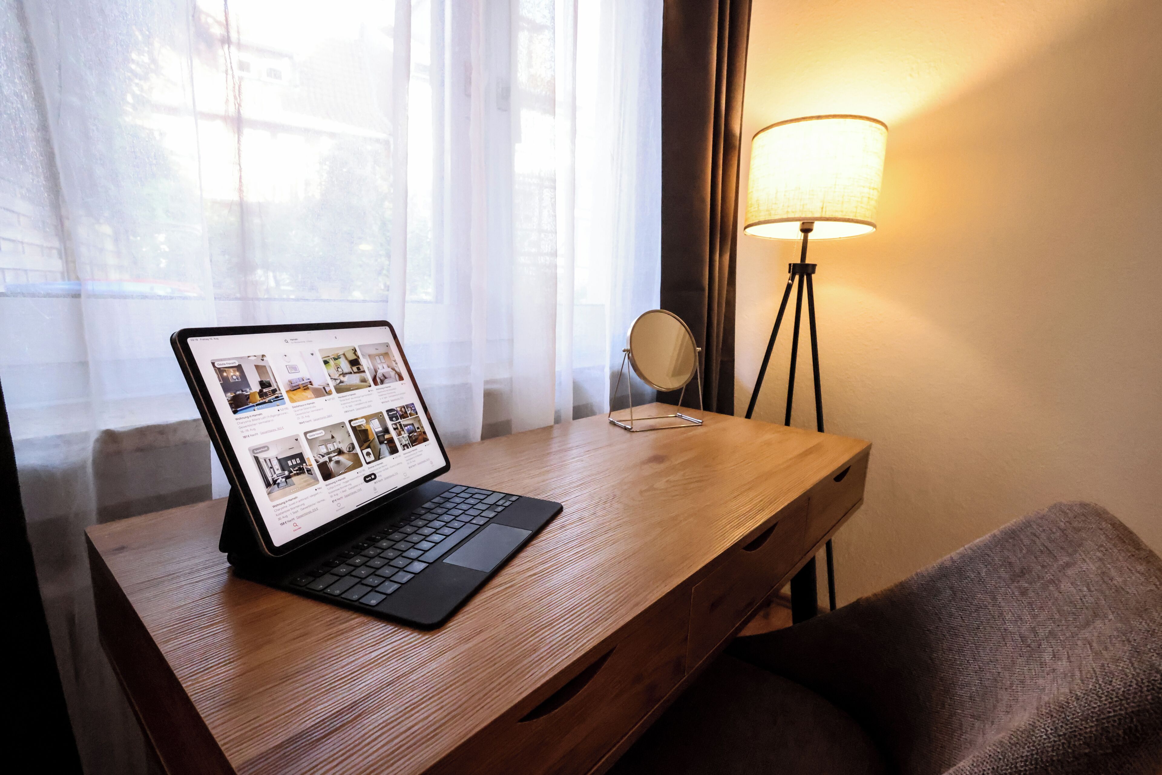 Ein Laptop auf einem Holztisch, nebenan eine Lampe und ein Spiegel.