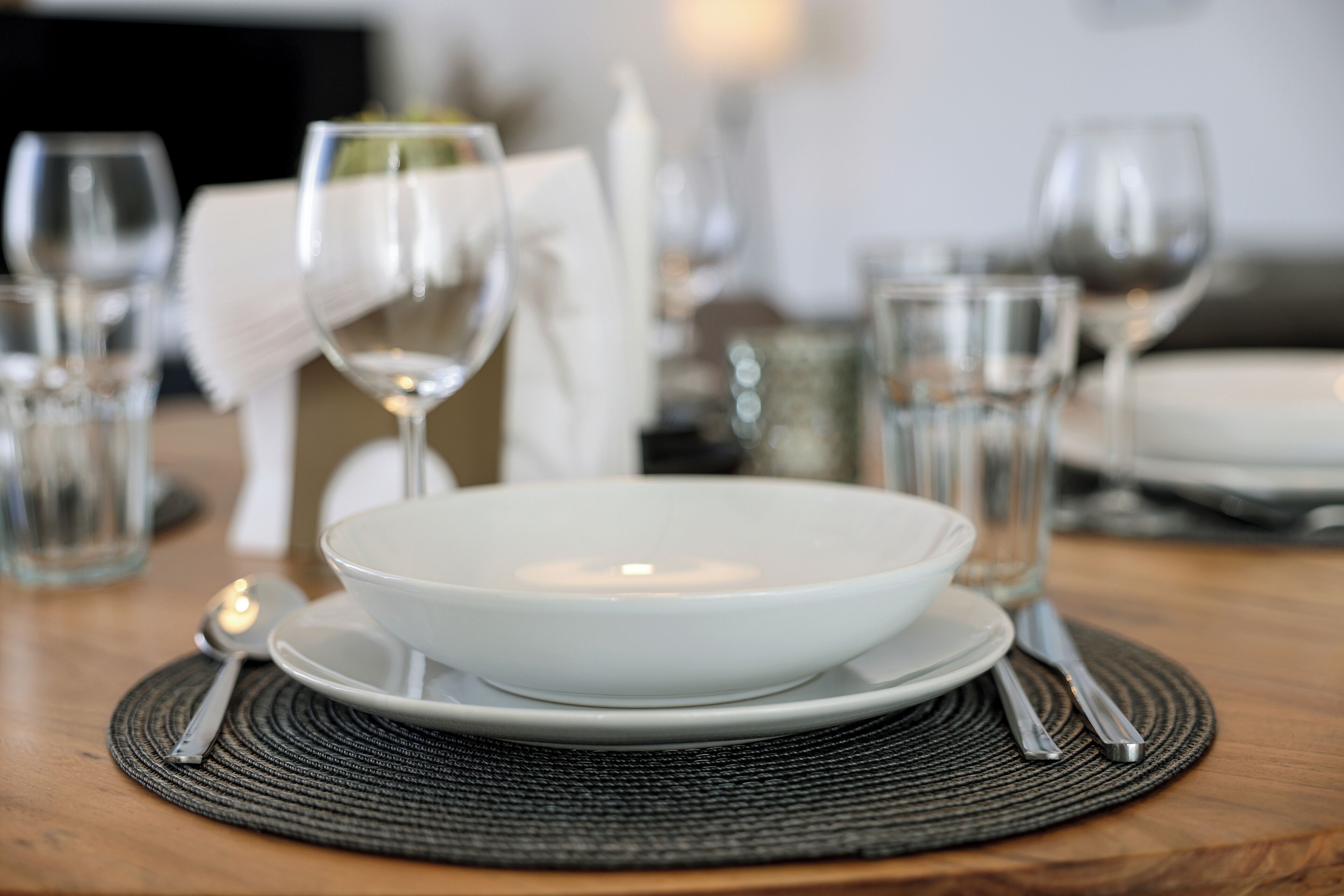 Une table à manger dressée avec un saladier blanc, des assiettes, des couverts et des verres.
