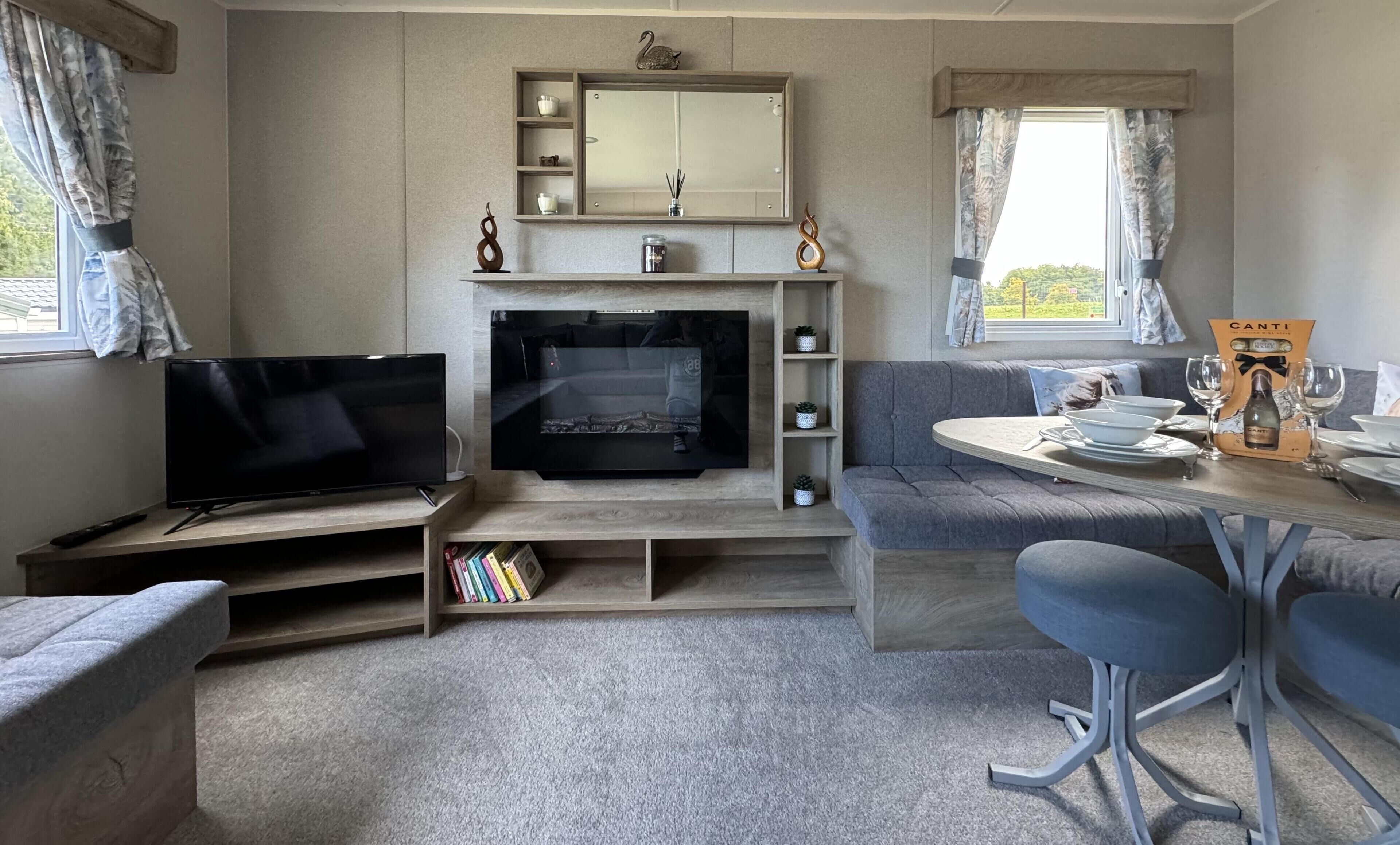 A cozy living room with a flat-screen TV, a fireplace, a sofa, a dining table with chairs, and a bookshelf.