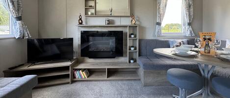 A cozy living room with a flat-screen TV, a fireplace, a sofa, a dining table with chairs, and a bookshelf.