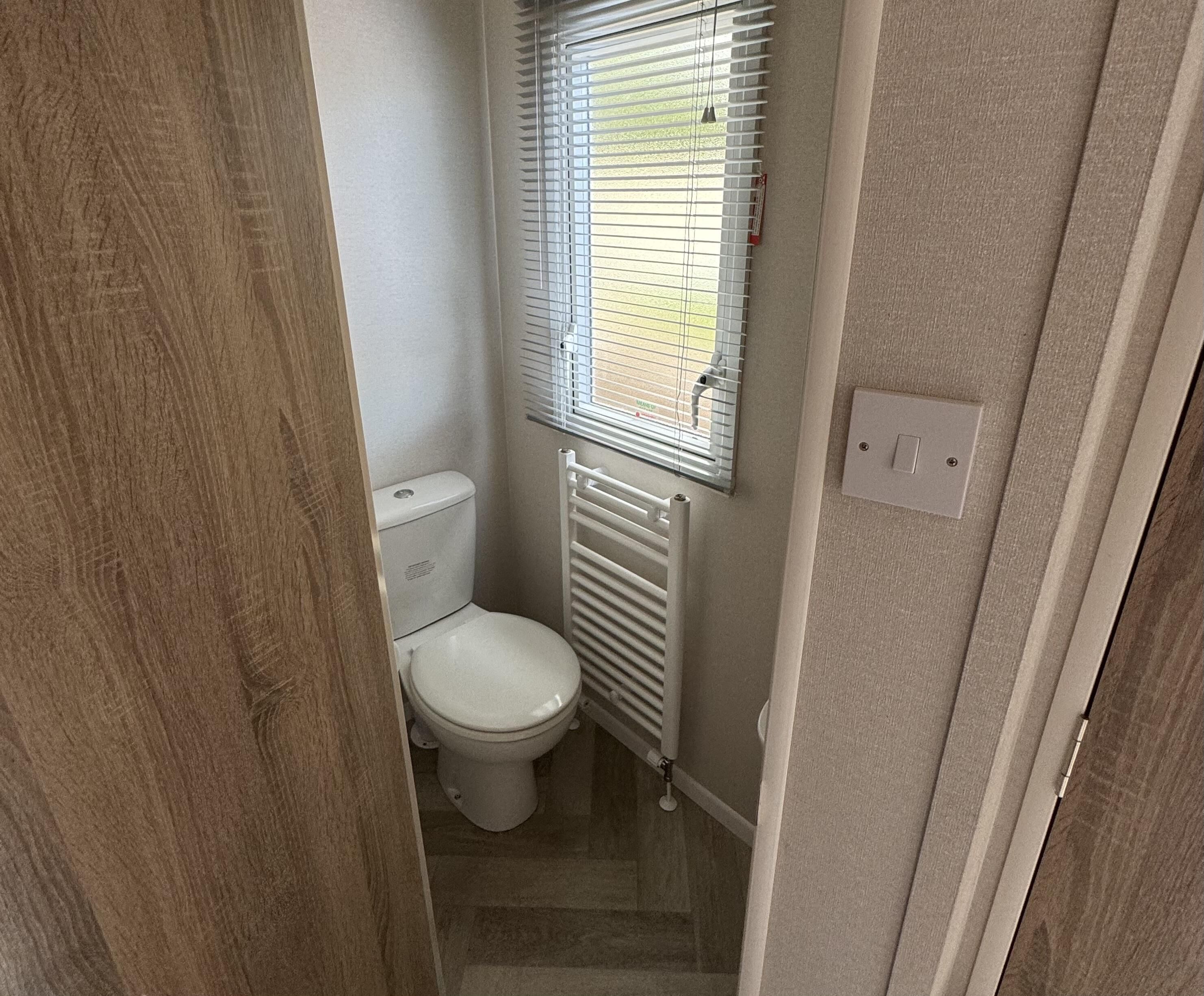 A compact bathroom with a toilet, a radiator, and a window with blinds.
