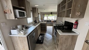 A modern kitchen with wooden cabinets, a microwave, a stove, and a sink. - West Lawn 47 Haggerston Castle Paddock Views (Berwick-upon-Tweed)