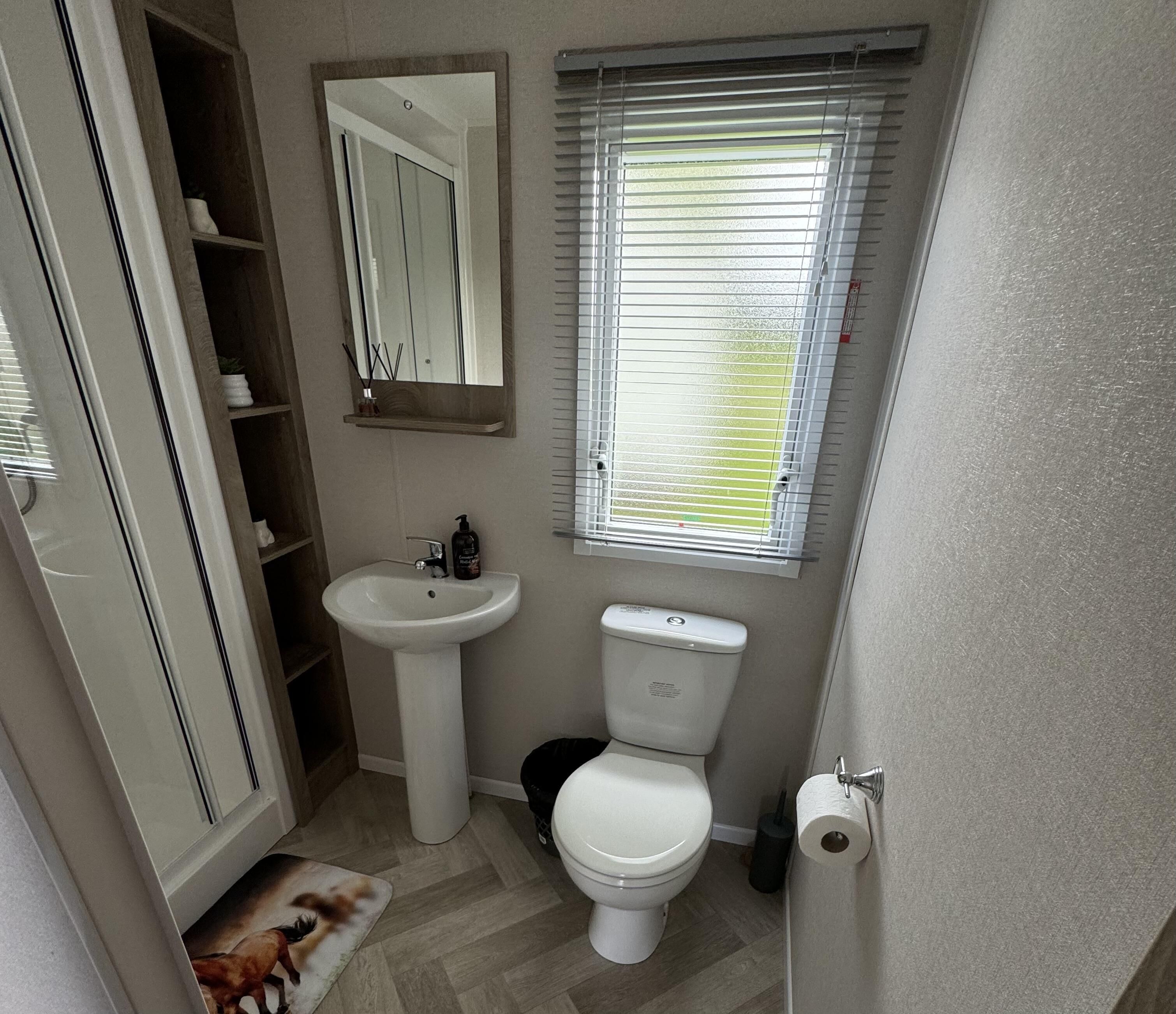 Une petite salle de bain comprenant un lavabo sur colonne, des toilettes et une fenêtre avec des stores.