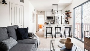 A modern kitchen with white cabinets, a microwave, and a coffee machine. There is a gray sofa with black cushions in the living area. - DTC One Bed Condo, Pool, Gym, Comfort (Greenwood Village)