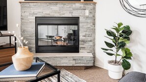 A modern living room with a stone fireplace, a wooden table with a vase, and a potted plant. - DTC One Bed Condo, Pool, Gym, Comfort (Greenwood Village)