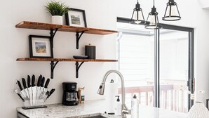 A kitchen with a sink, coffee maker, and knife set. There are wooden shelves above the counter with a plant and picture frames. - DTC One Bed Condo, Pool, Gym, Comfort (Greenwood Village)