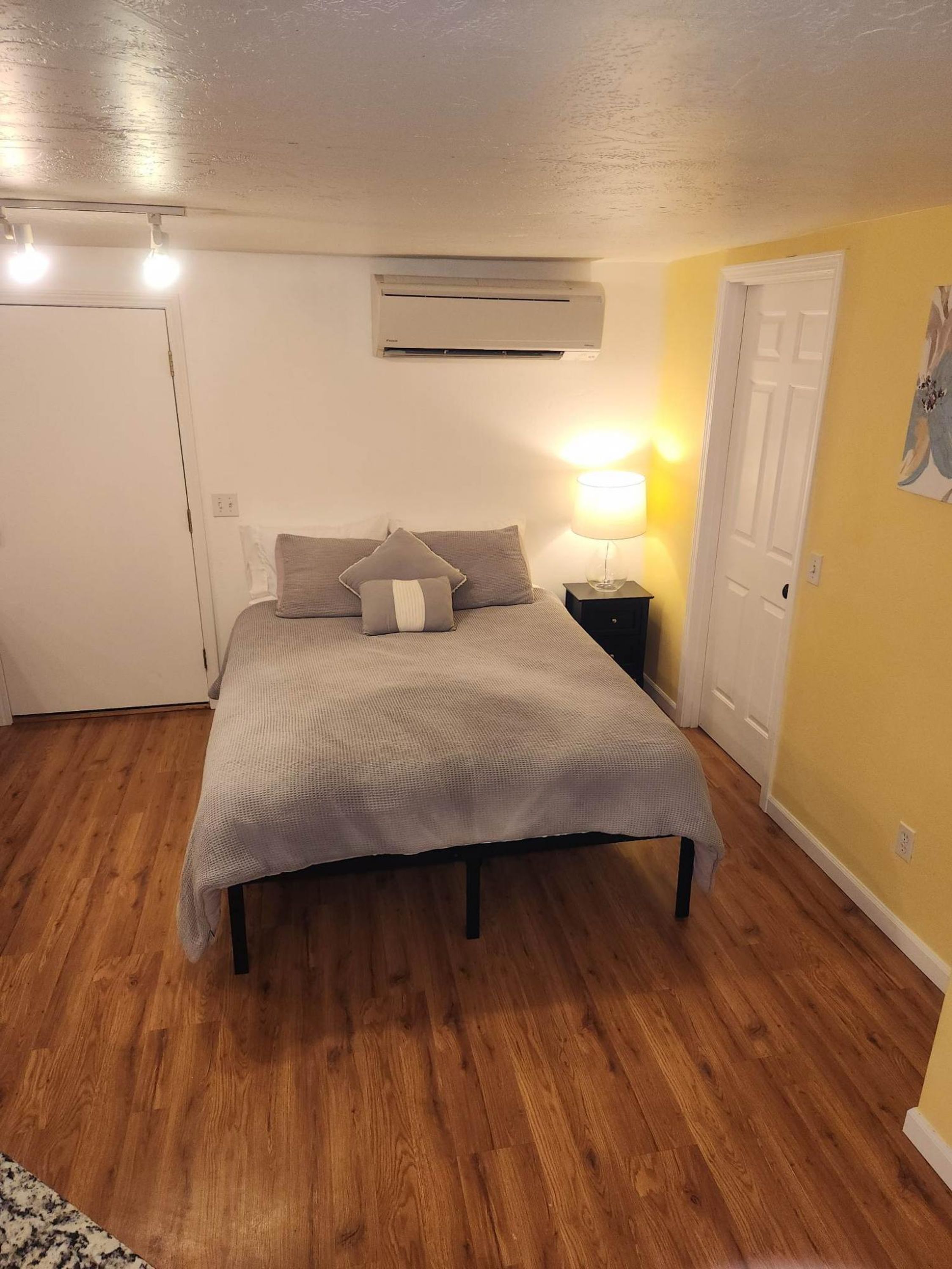 A bedroom with a bed, a nightstand, an air conditioner, and a door.