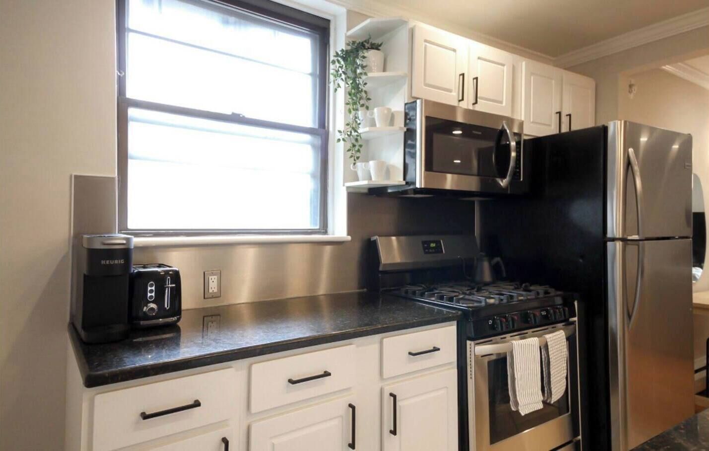 Una cocina moderna con gabinetes blancos, un refrigerador negro, una estufa y una cafetera.