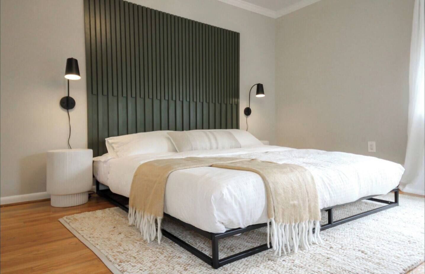 Une chambre à coucher moderne avec un lit, des lampes de chevet, un panneau décoratif au mur et un tapis blanc.