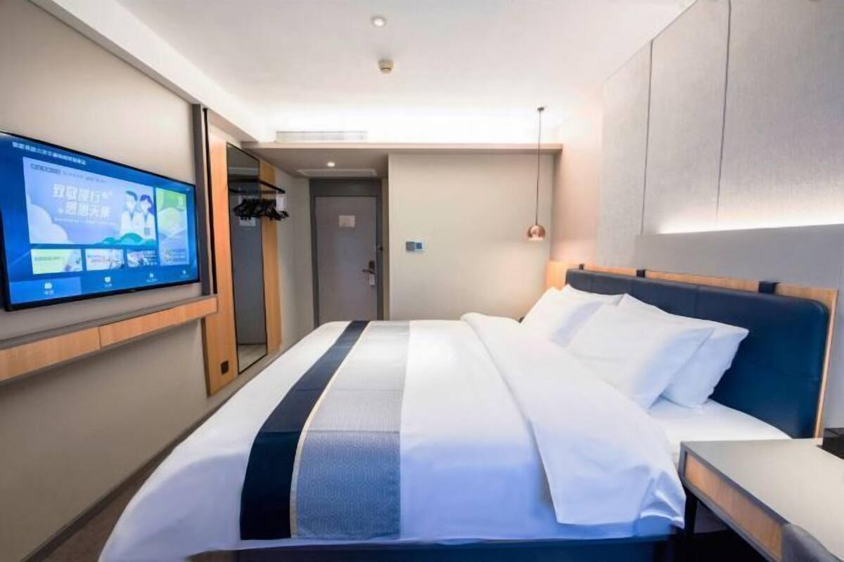 Une chambre d’hôtel comprenant un lit, un téléviseur fixé au mur, une table de chevet et une porte donnant sur une salle de bain.