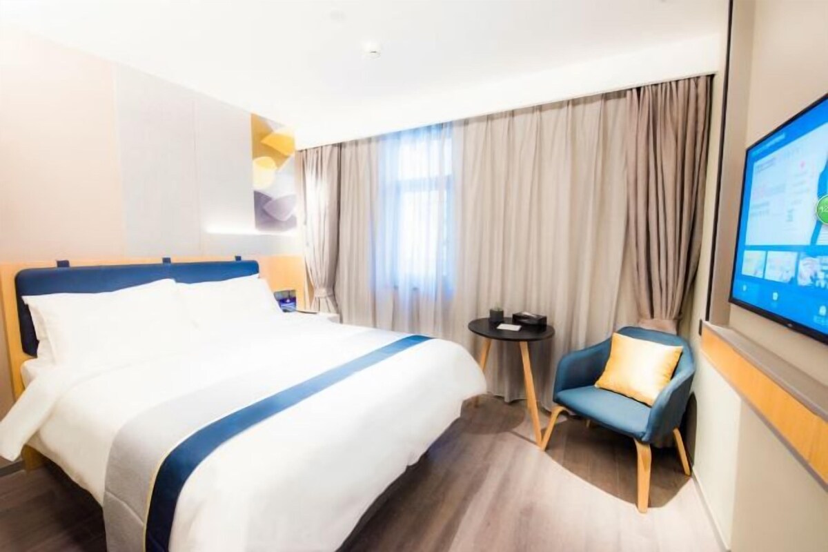 A hotel room with a large bed, a small table, a chair, and a TV mounted on the wall.