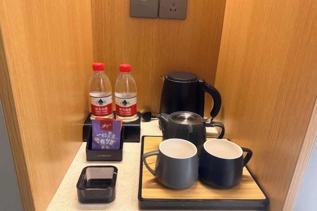 A small kitchenette with a coffee maker, two mugs, two bottles of water, a tea box, and a small tray.
