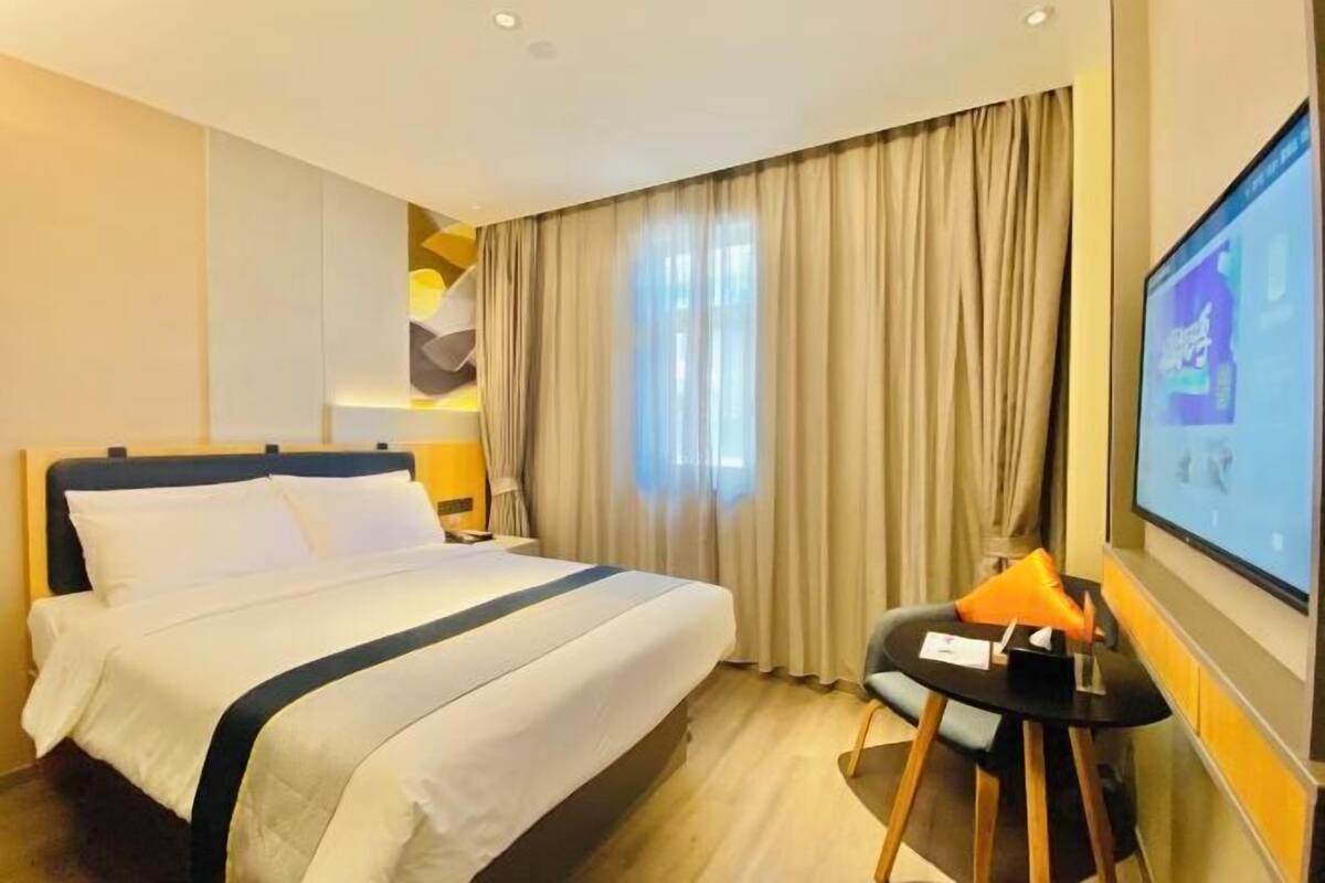 Une chambre d’hôtel avec un lit, un bureau, une chaise, une télévision et des rideaux.