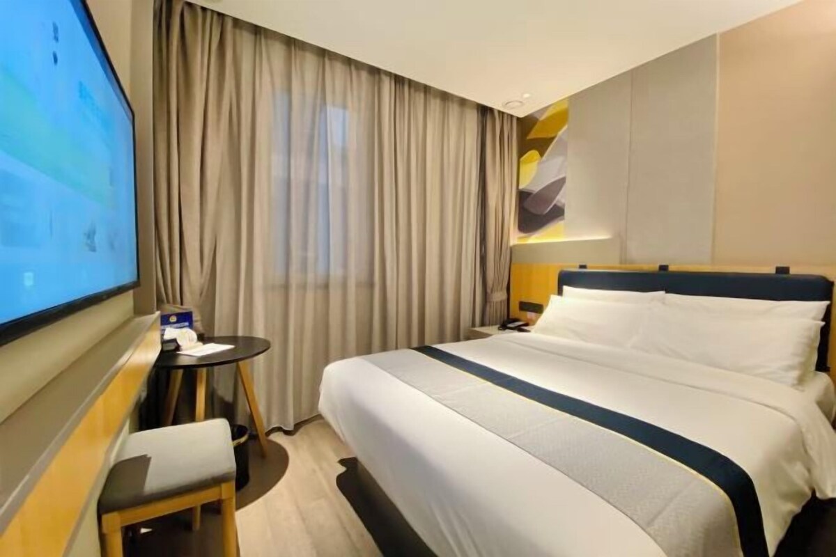 A hotel room with a bed, a desk, a chair, a TV, and curtains.