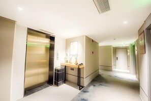 A hotel hallway with an elevator, a small desk with a telephone, and a trash bin. - Homeinn Selected Hotel (Beijing Beixinqiao Nanluoguxiang) (Beijing)