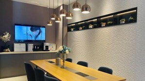 A modern dining area with a long wooden table, black chairs, a television, and a wall-mounted shelf with decorative items. - Homeinn Selected Hotel (Beijing Beixinqiao Nanluoguxiang) (Beijing)