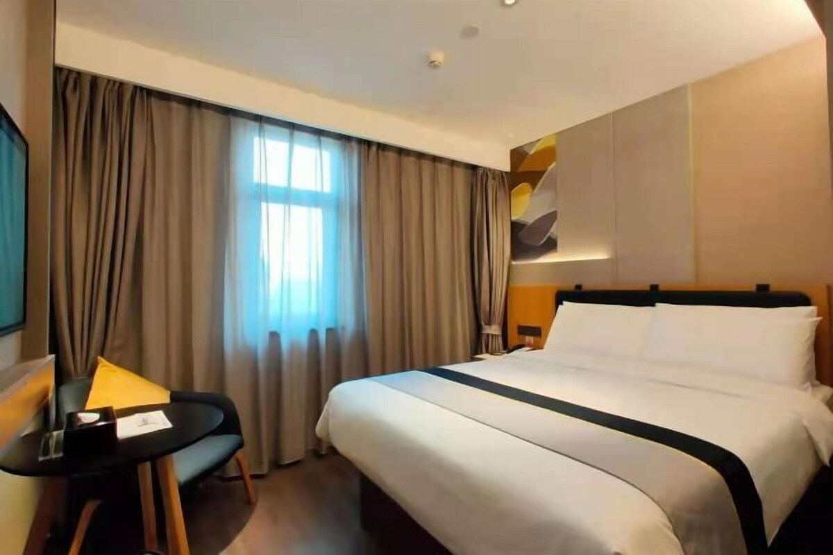 A hotel room with a large bed, a desk, and a window with curtains.